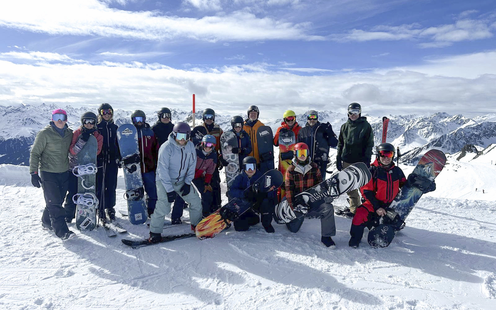 Gruppe von Snowboardfahrern auf einer Skipiste in Leogang mit Ausblick auf verschneite Berge.