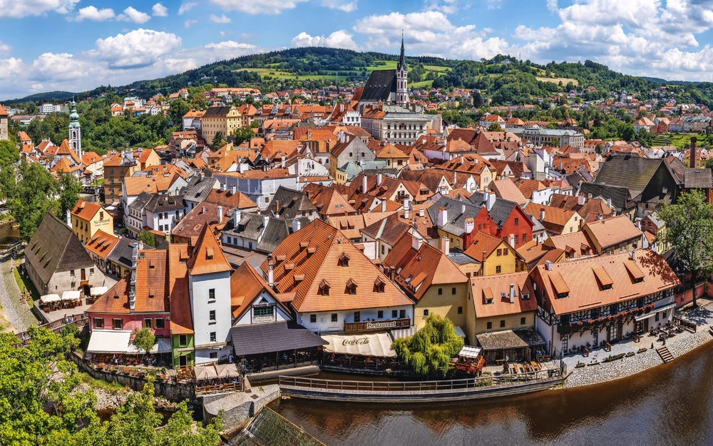 Panoramablick auf eine Altstadt mit Fluss und Hügeln im Hintergrund.