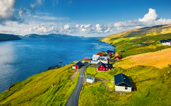 Panoramablick im Sommer aus einer Drohne auf das Dorf Kirkjubour mit der Insel Hestur im Hintergrund