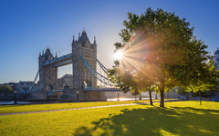 London, Großbritannien – berühmte Tower Bridge bei Sonnenaufgang mit Sonnenlicht, Bäumen, blauem Himmel und grünem Gras