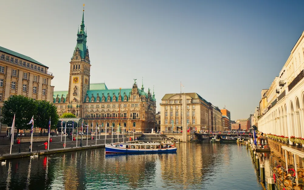Hamburger Rathaus mit Wasserkanal und Boot im Vordergrund bei Sonnenschein.