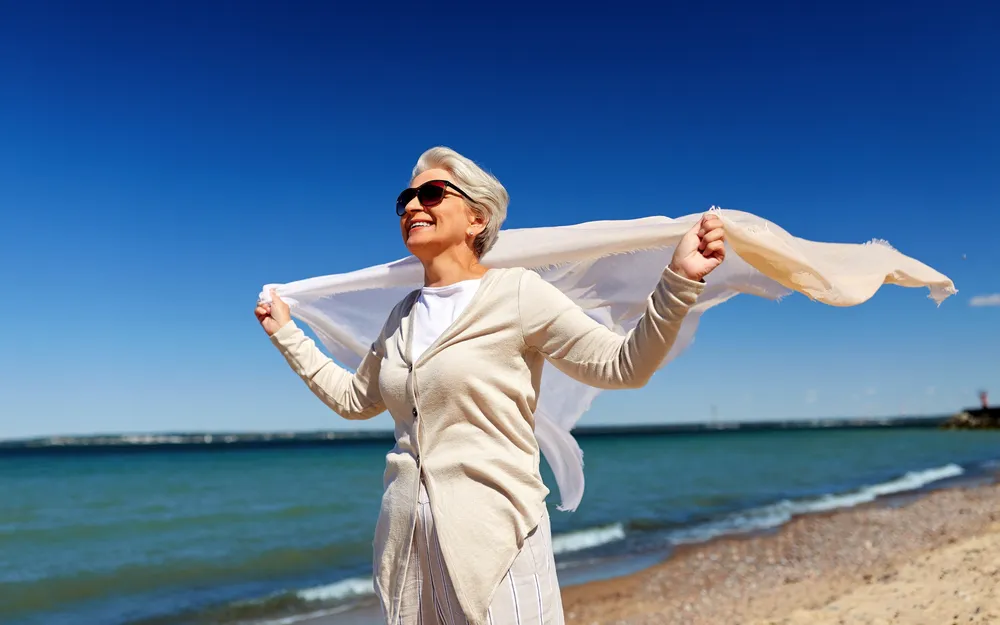 Ältere Frau mit Schal am Strand bei sonnigem Wetter.