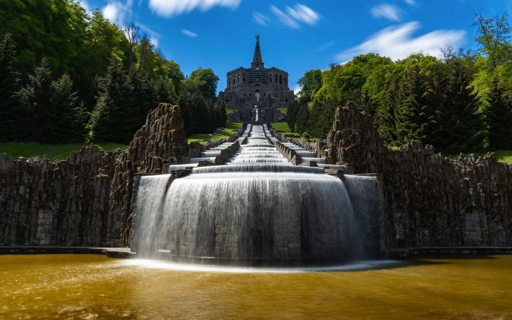 Wasserspiele vor dem Herkules-Denkmal im Bergpark Wilhelmshöhe, umgeben von Bäumen.