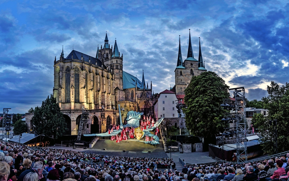 Open-Air-Theateraufführung vor einem großen gotischen Dom bei Abenddämmerung.