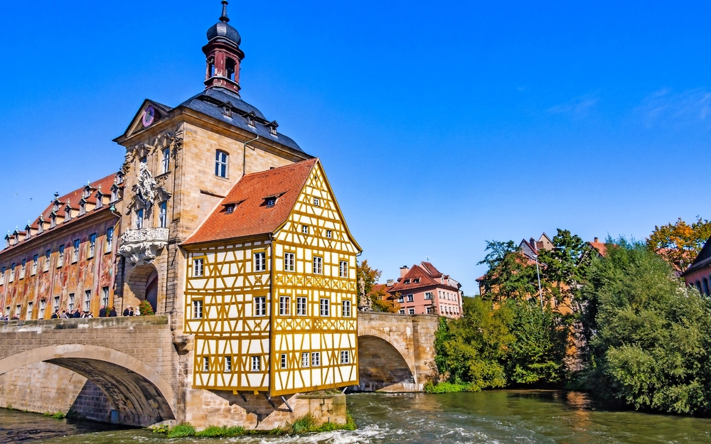 Fachwerkhaus auf einer Brücke über einem Fluss, blauer Himmel im Hintergrund.