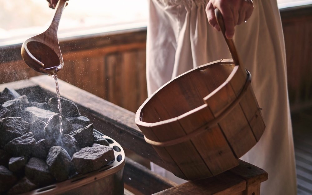 Mann gießt Wasser auf heiße Steine in der Sauna.