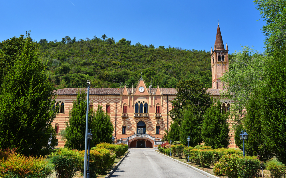 Historisches Gebäude mit Turm vor grünem Hügel unter blauem Himmel.