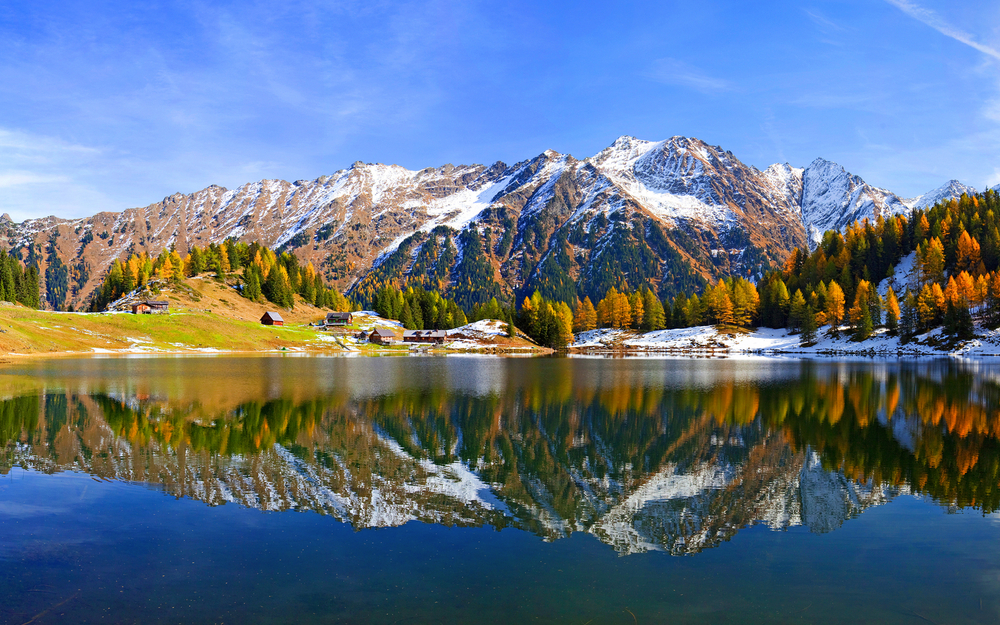 Bergsee mit herbstlichen Bäumen und schneebedeckten Bergen im Hintergrund
