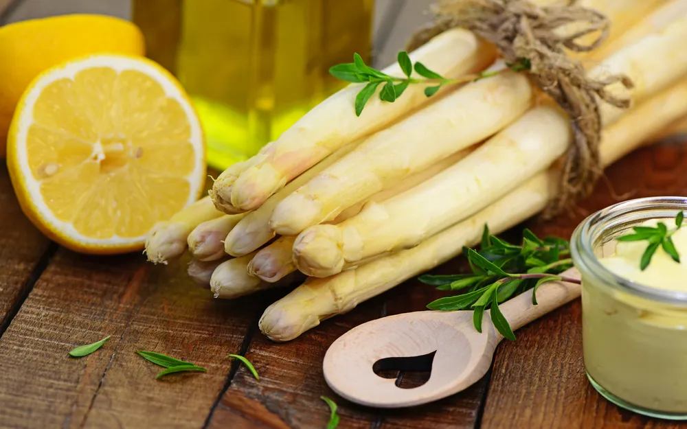 Weiße Spargelstangen mit frischem Zitronenstück und Sauce Hollandaise auf einem Holzbrett.