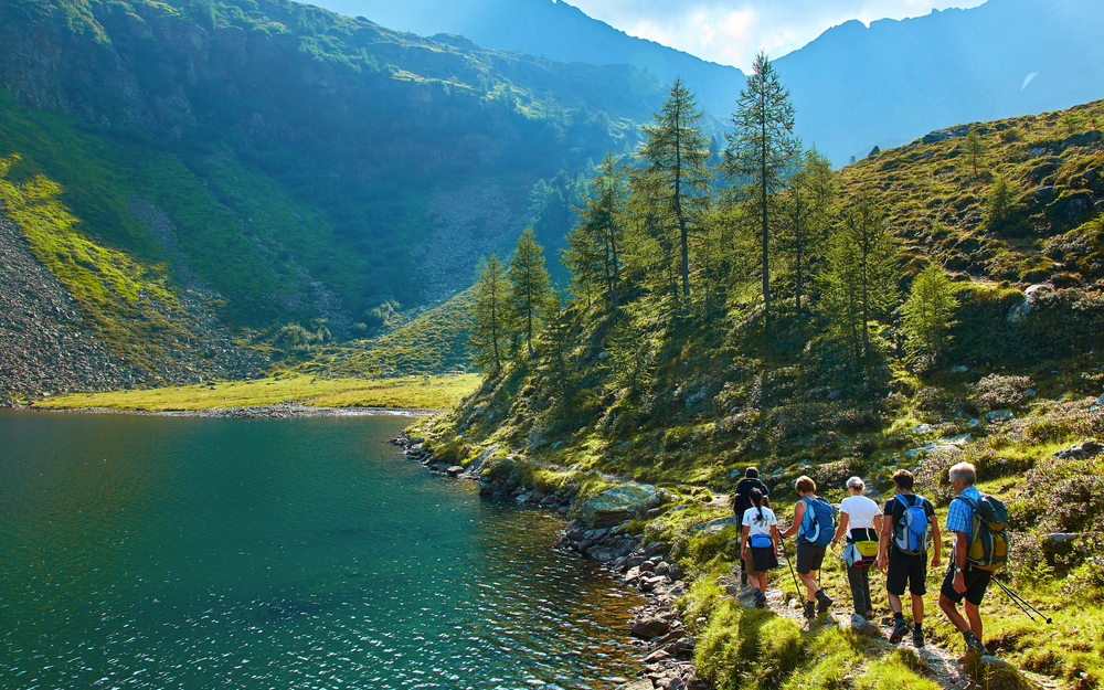 Gruppe von Menschen wandert entlang eines Bergsees in einer grünen Landschaft.