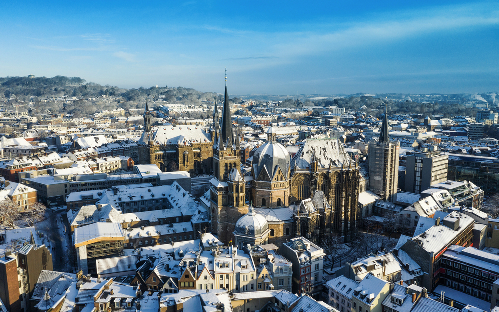 Luftaufnahme von Aachen im Winter mit schneebedeckten Dächern und dem Aachener Dom im Zentrum.