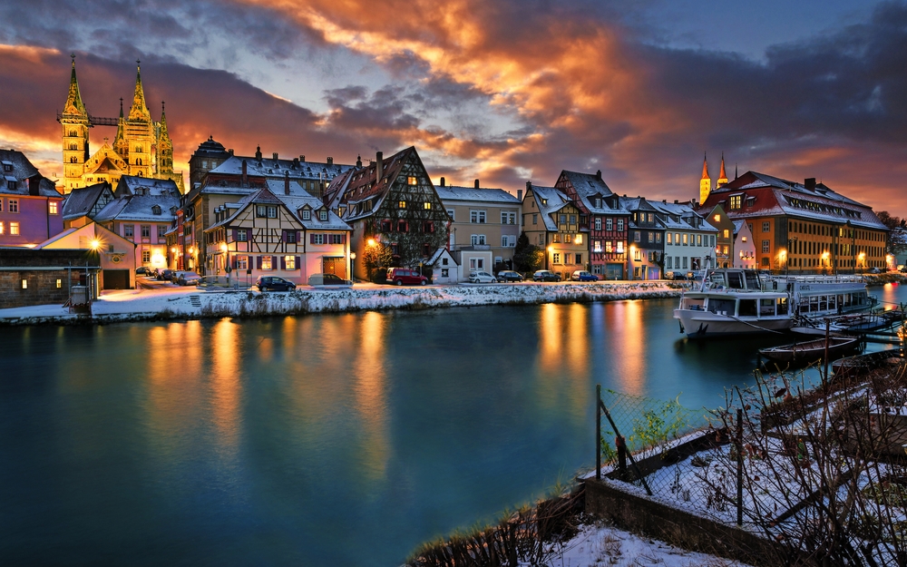 Altstadt am Flussufer mit beleuchteten, verschneiten Häusern bei Sonnenuntergang.
