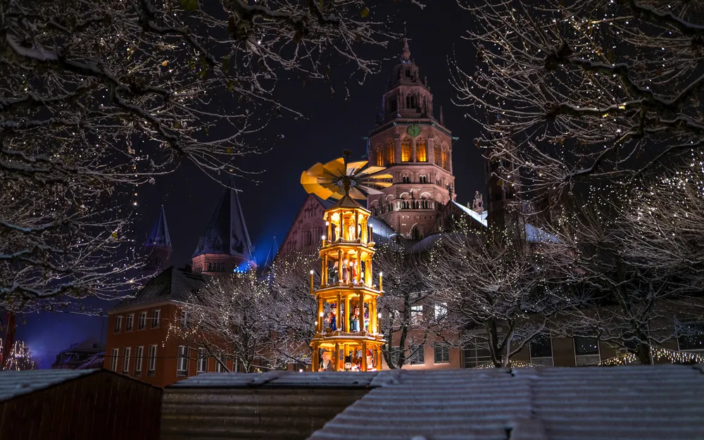 Beleuchtete Weihnachtspyramide vor einer Kathedrale im Schnee bei Nacht.