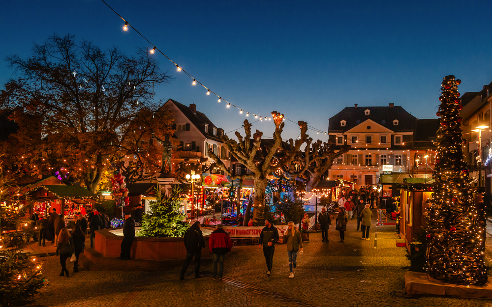 Weihnachtsmarkt mit Lichtern, Buden und Menschen bei Abenddämmerung.