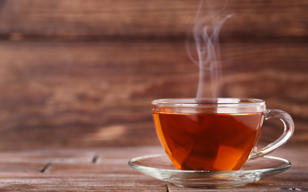 Tasse Tee mit Dampf auf braunem Holztisch